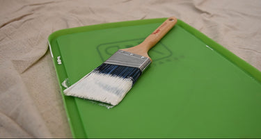 Green paint tray lid with wet paint brush and white paint
